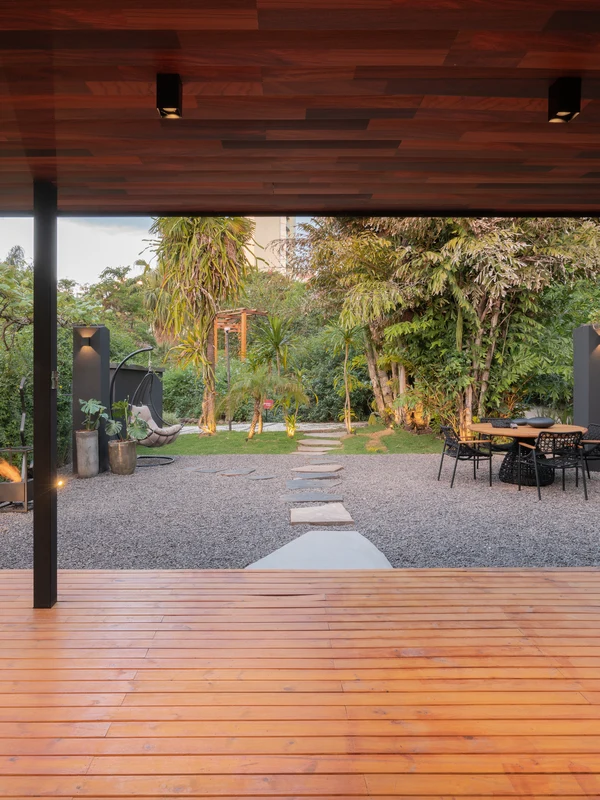 Deck de madeira com forro e lareira ecológica Loft Round Somer, jardim paisagístico com caminho de pedras e vegetação tropical