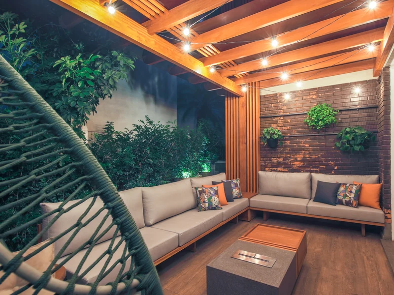 Queimador QS-1500 QS-1500-A da Somer embutido em mesa de centro de granito sobre estrutura de madeira em pergola residencial noturna com sofá em L, balanço suspenso e iluminação pendente cálida, projeto Luma Trevisan, foto Ricardo Fabrello
