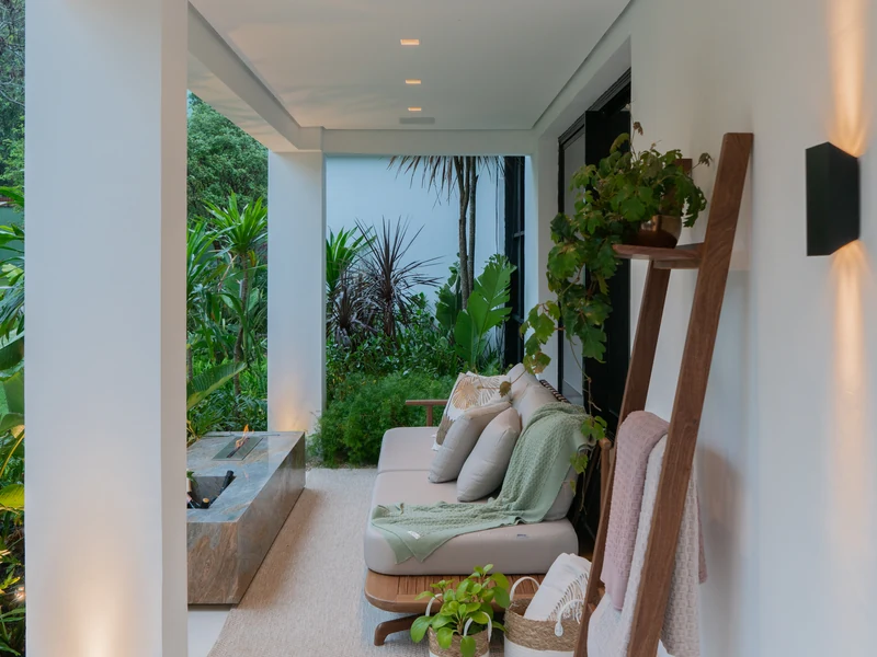 Queimador QS-2000 QS-2000-A da Somer embutido em mesa de pedra em varanda residencial coberta de alto padrão com sofá, almofadas, escada decorativa em madeira tratada com cestos e plantas, vegetação tropical ao fundo.