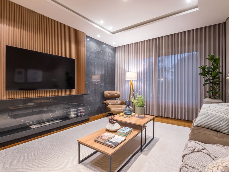 Queimador QS-3000 QS-3000-A da Somer embutido em painel de mármore preto sob TV de madeira ripada em sala de estar residencial de alto padrão, com poltrona em couro caramelo e abajur tripé com cúpula clara.