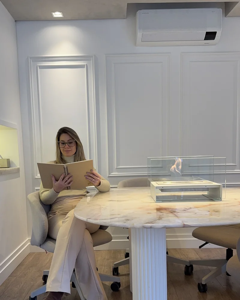 Mulher na sala de estar lendo caderno ao lado da Lareira GO! Branca da Somer sobre mesa de mármore em ambiente com painéis brancos e decoração neutra
